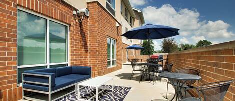 An outdoor patio with a blue sofa, metal chairs, a table, and a patterned rug.
