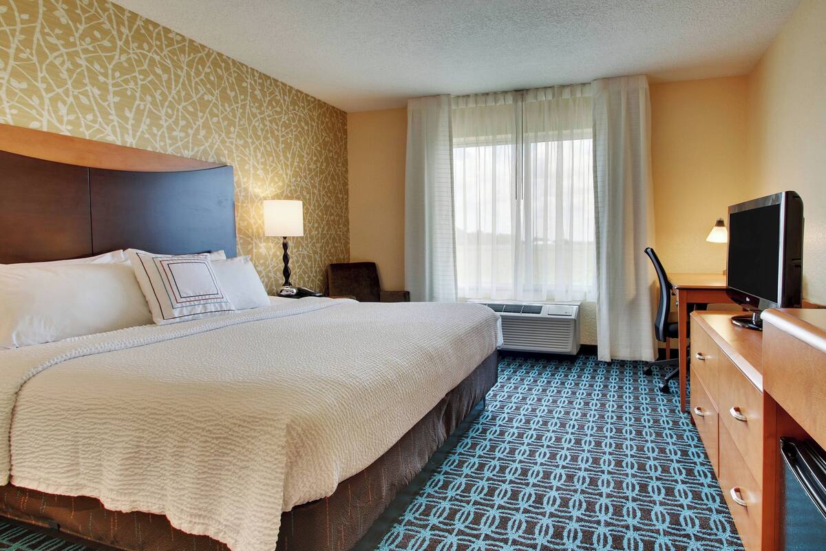 Ein Hotelzimmer mit einem großen Bett, einem Fernseher, einem Schreibtisch und einem Schminktisch.