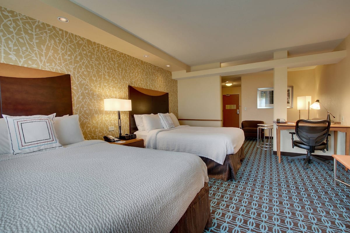 Ein Hotelzimmer mit zwei Betten, einem Schreibtisch, einem Stuhl und einem gemusterten Teppich.