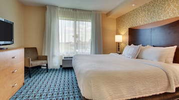 A hotel room with a large bed, a TV, a desk, a chair, and a window with curtains.