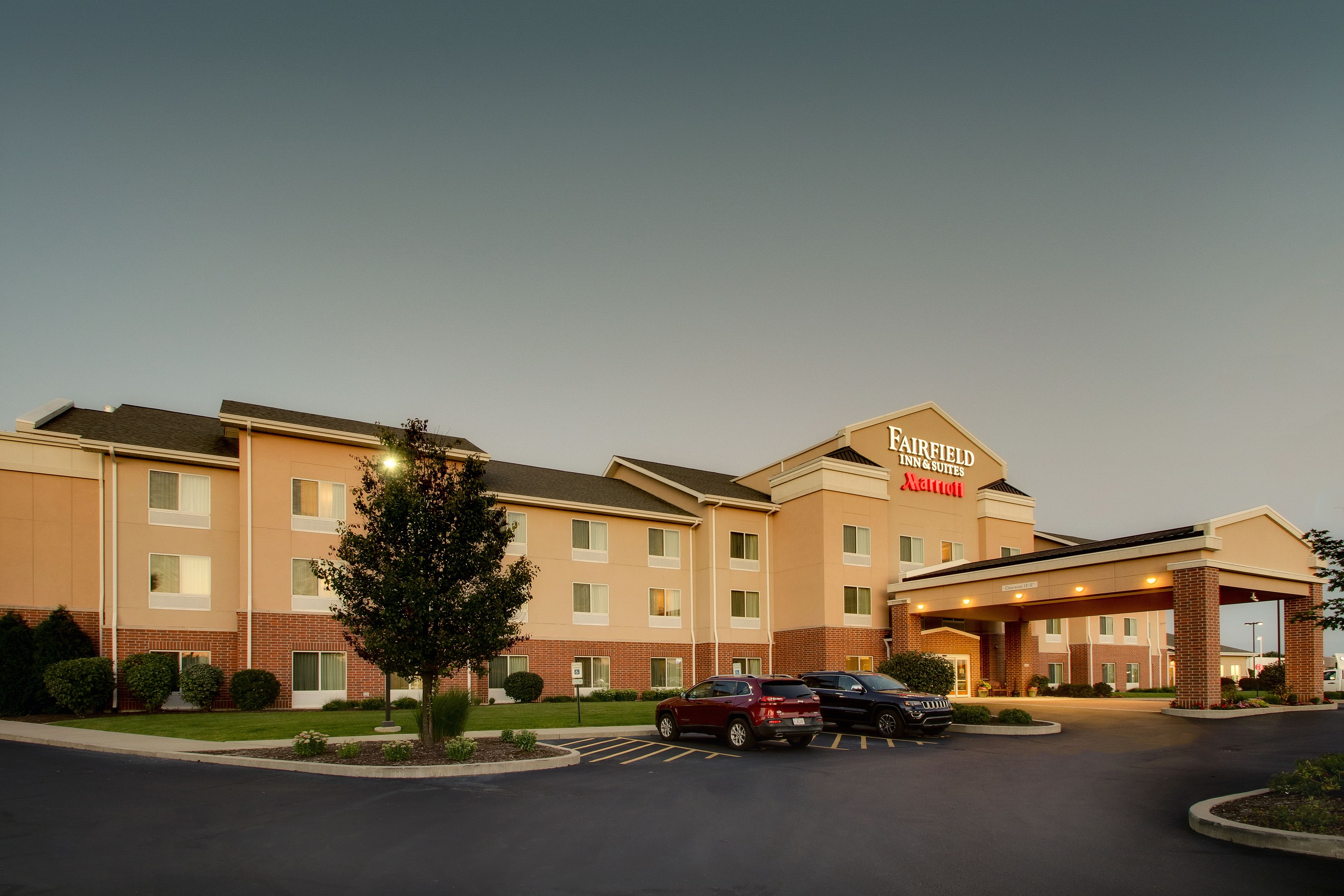 Un hotel Fairfield Inn & Suites con fachada de ladrillo, múltiples ventanas y un estacionamiento con varios autos.