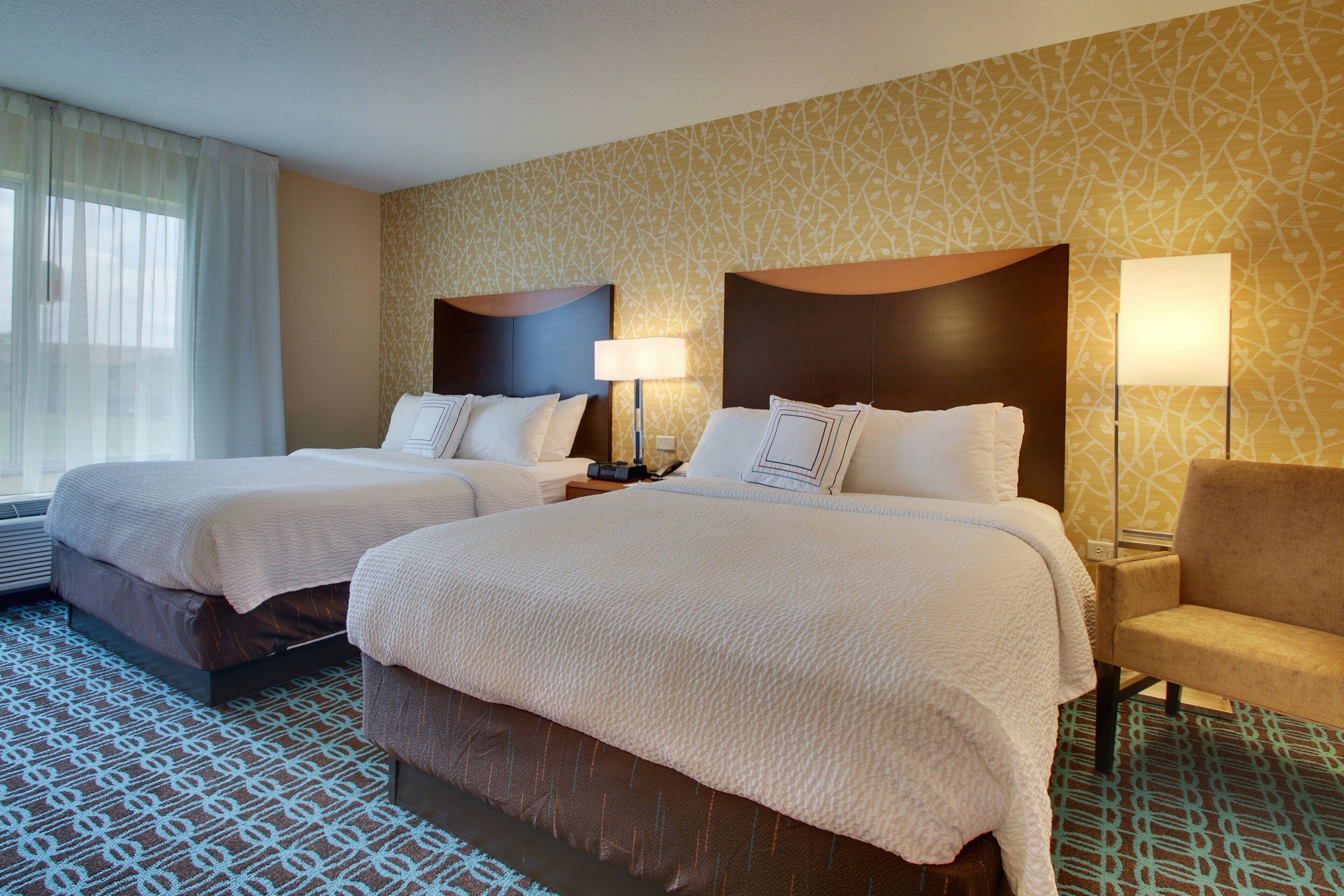Habitación de hotel con dos camas, una silla y una alfombra estampada.