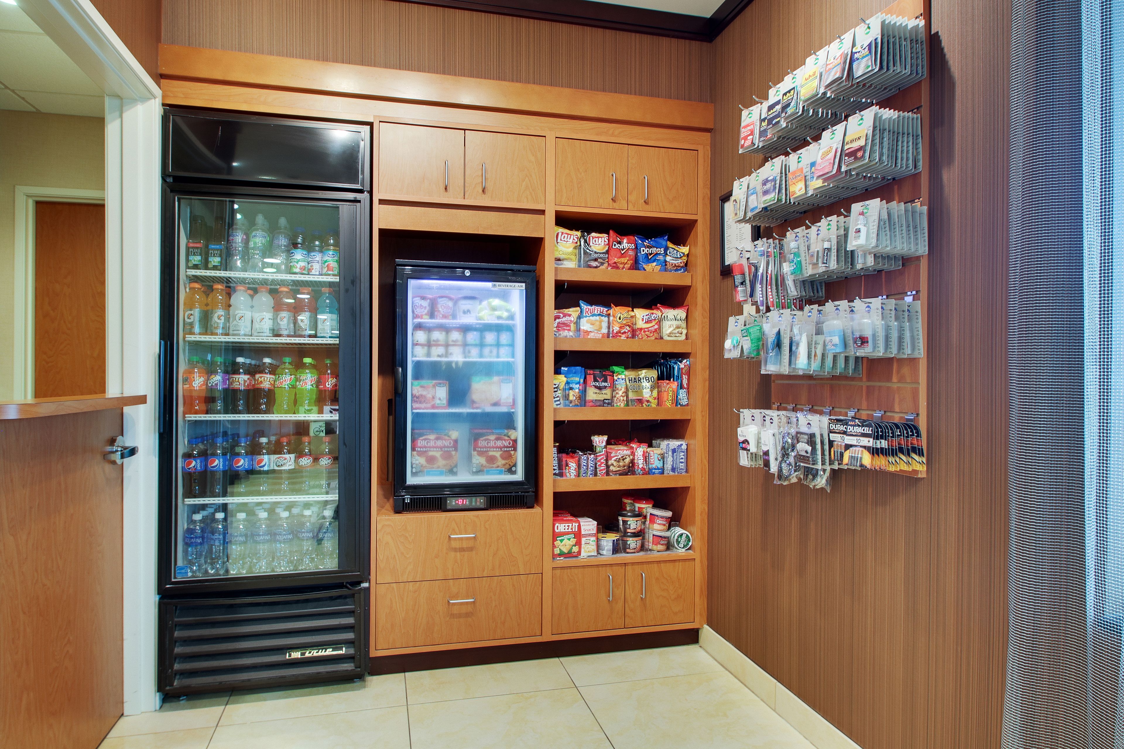 A vending area with a refrigerator, shelves stocked with snacks, and a display of bottled water and other beverages.