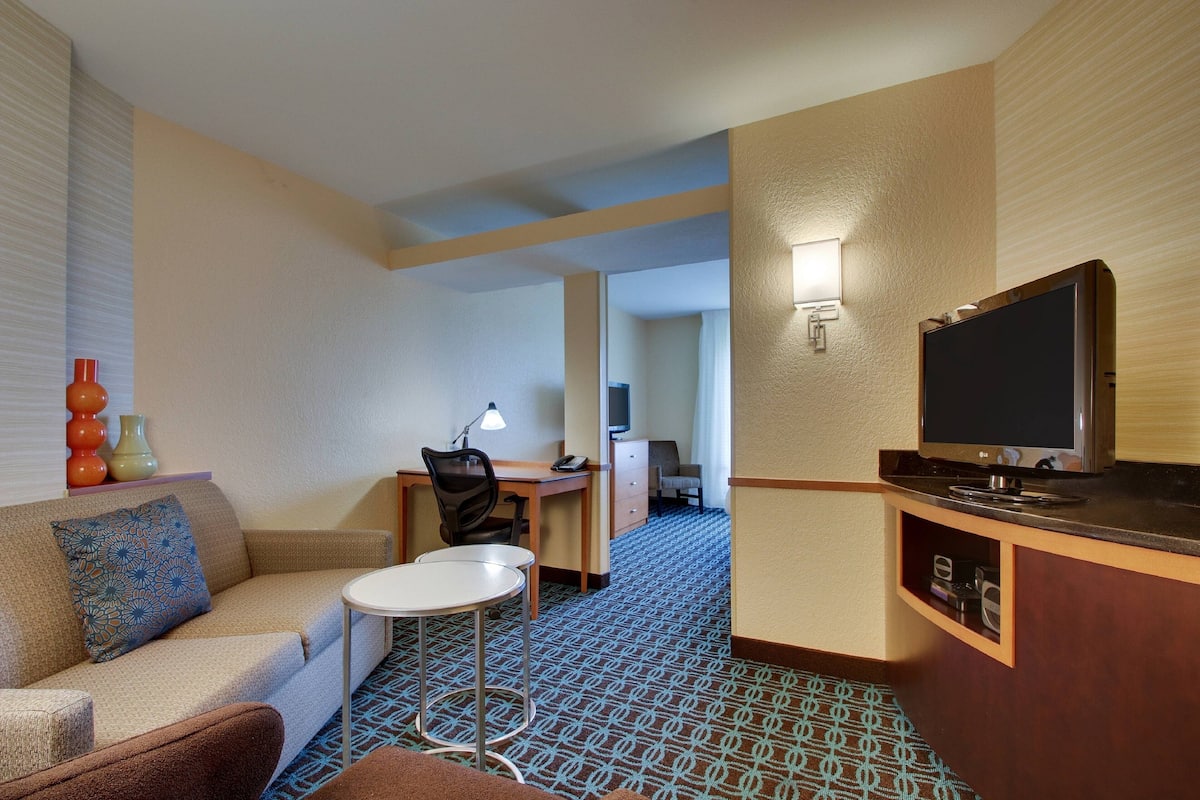 Ein Hotelzimmer mit Sofa, einem kleinen Tisch, einem Schreibtisch mit Stuhl, einem Fernseher und einer Minibar.