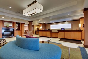 A modern hotel lobby with a blue sofa, a reception desk, a kitchen area, and a fireplace.