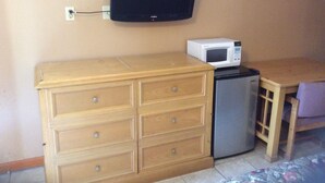 A kitchenette with a microwave, a small refrigerator, a wooden cabinet with drawers, and a television mounted on the wall. - Budget Inn And Suites (Abbeville)