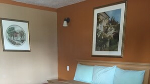 A hotel room with a large bed, a red and beige bedspread, two light blue pillows, and two framed pictures on the walls. - Budget Inn And Suites (Abbeville)