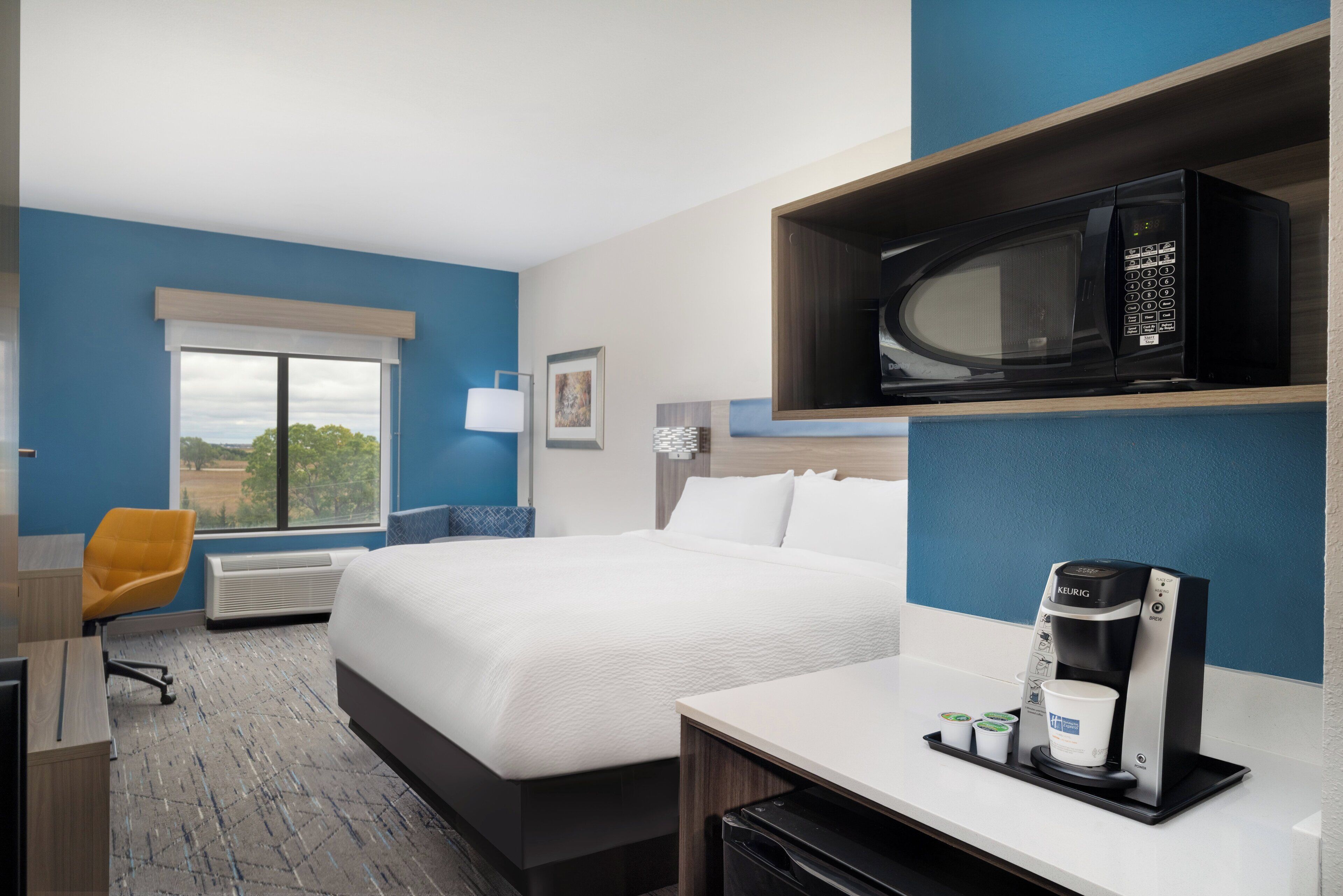 Una habitación de hotel con una cama, un escritorio con cafetera, microondas y una silla.