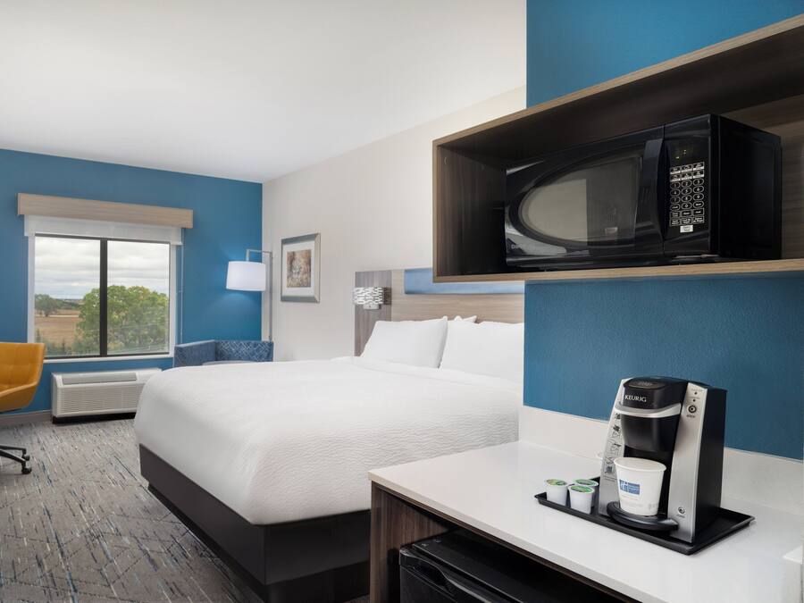 Una habitación de hotel con una cama, un escritorio con cafetera, microondas y una silla.