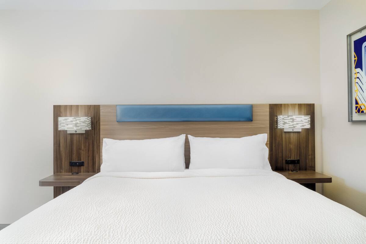 A hotel room with a large bed, wooden headboard, two bedside tables with lamps, and a blue accent wall.