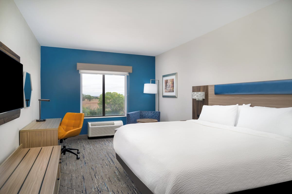 A hotel room with a large bed, a desk with a chair, a window with a view, and a mounted TV.