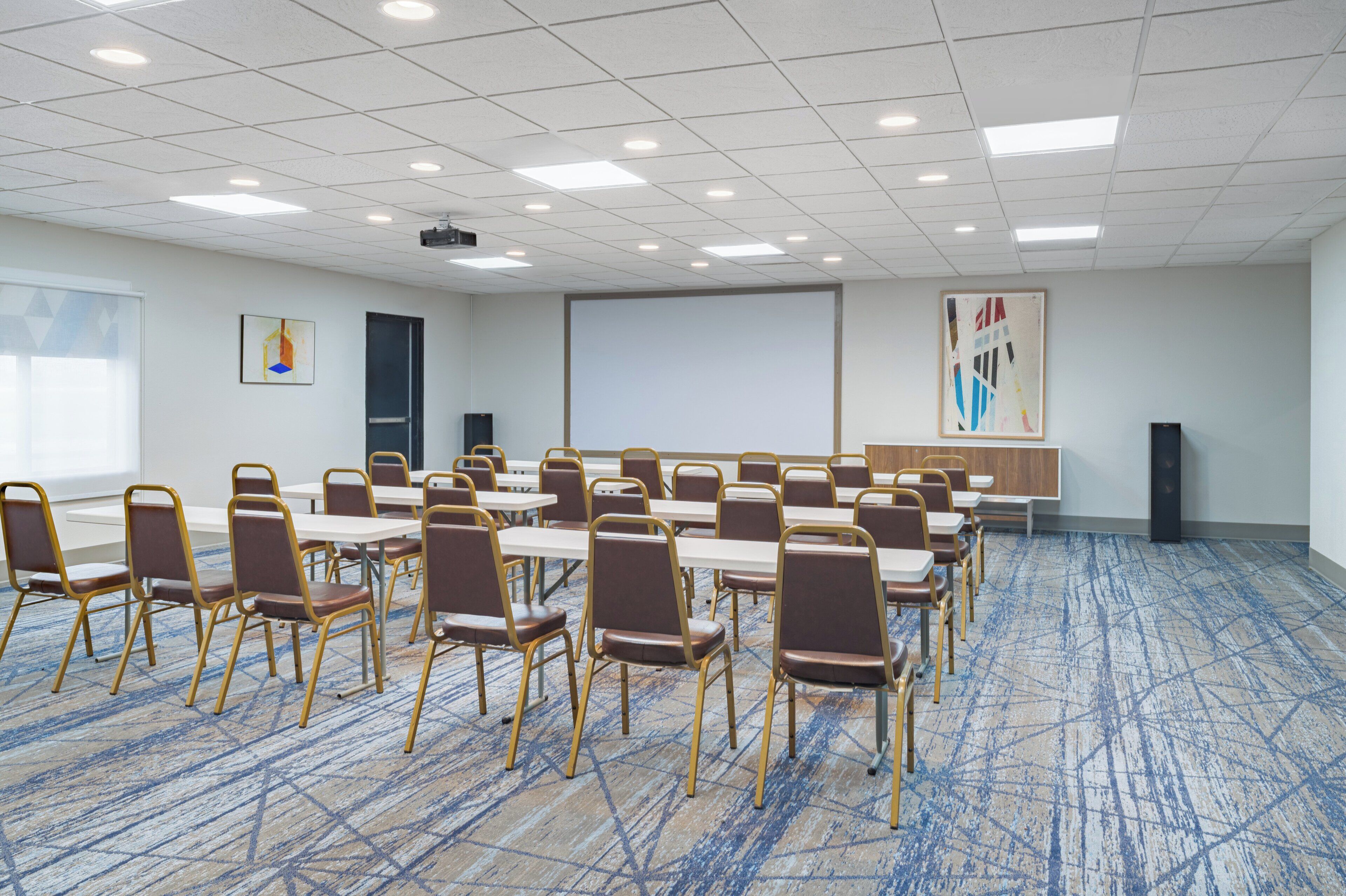 A conference room with tables and chairs, a projector screen, and a large abstract painting on the wall.