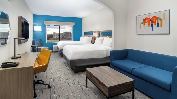 A hotel room with two beds, a desk, a chair, a sofa, and a painting on the wall. - Holiday Inn Express Hotel & Suites Pratt by IHG (Pratt)