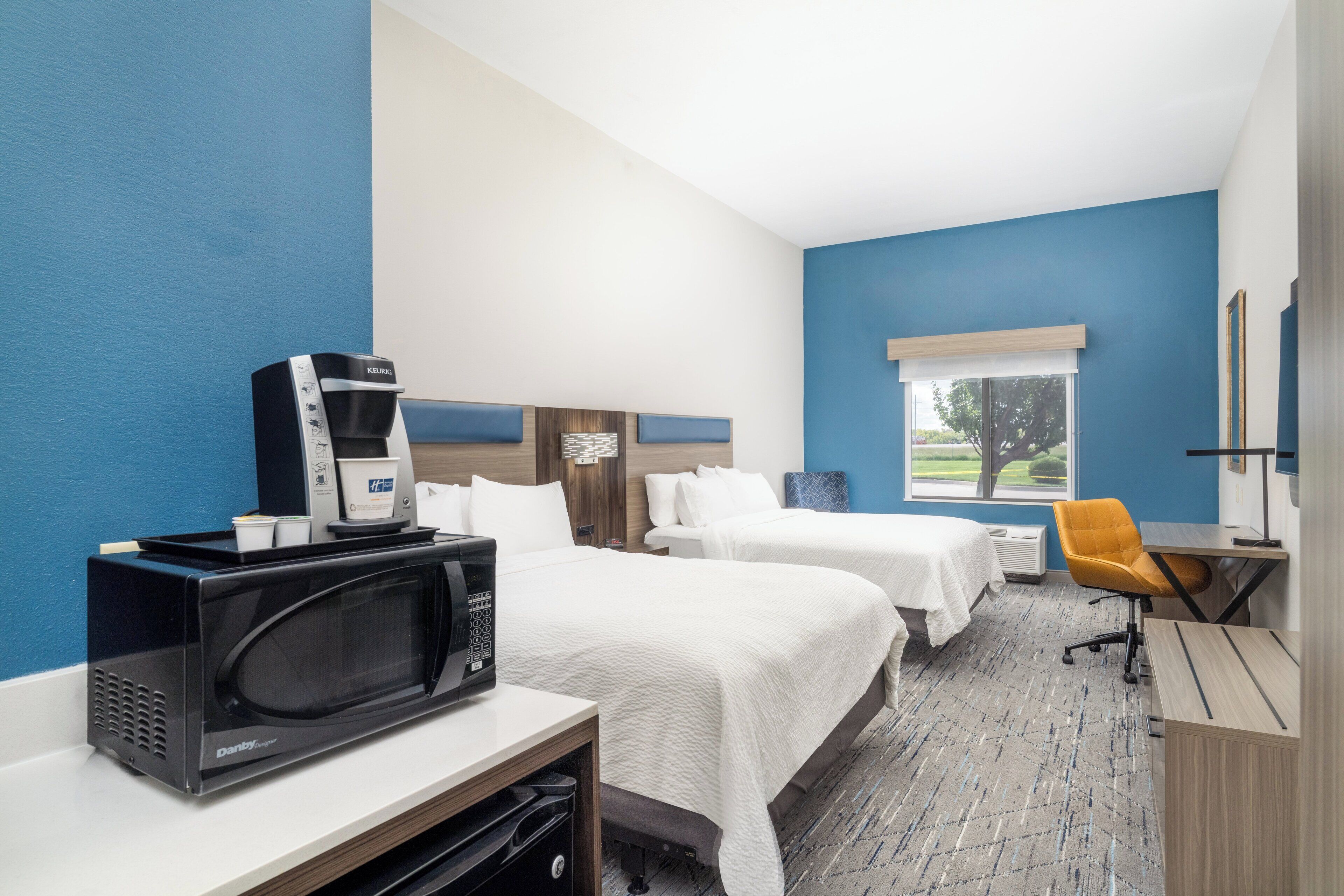 A hotel room with two beds, a microwave, a coffee maker, a desk, and a chair.