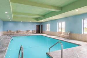 An indoor swimming pool with clear water, surrounded by chairs and a door leading to another room.