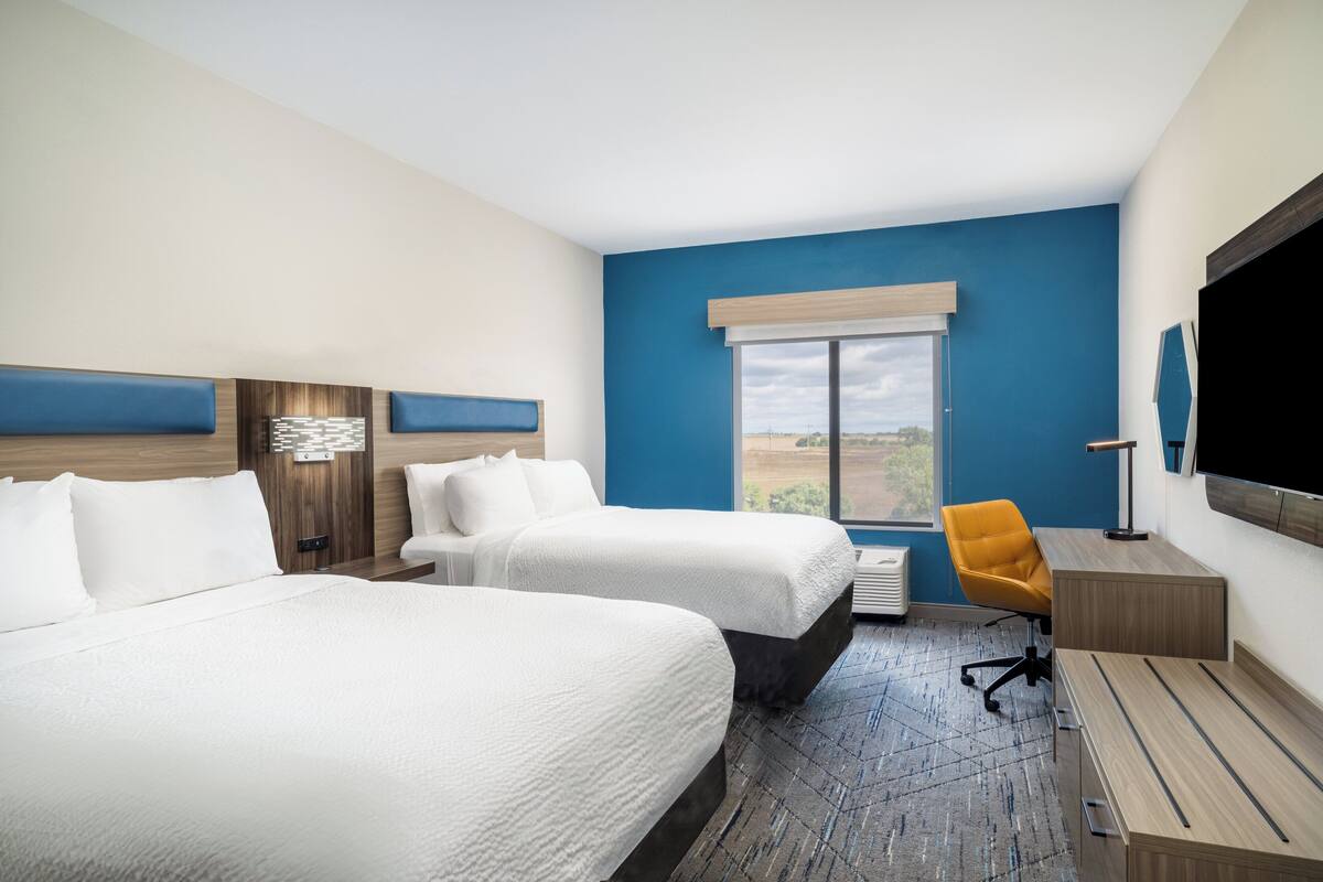 A hotel room with two beds, a desk, a chair, a TV, and a window with a view.