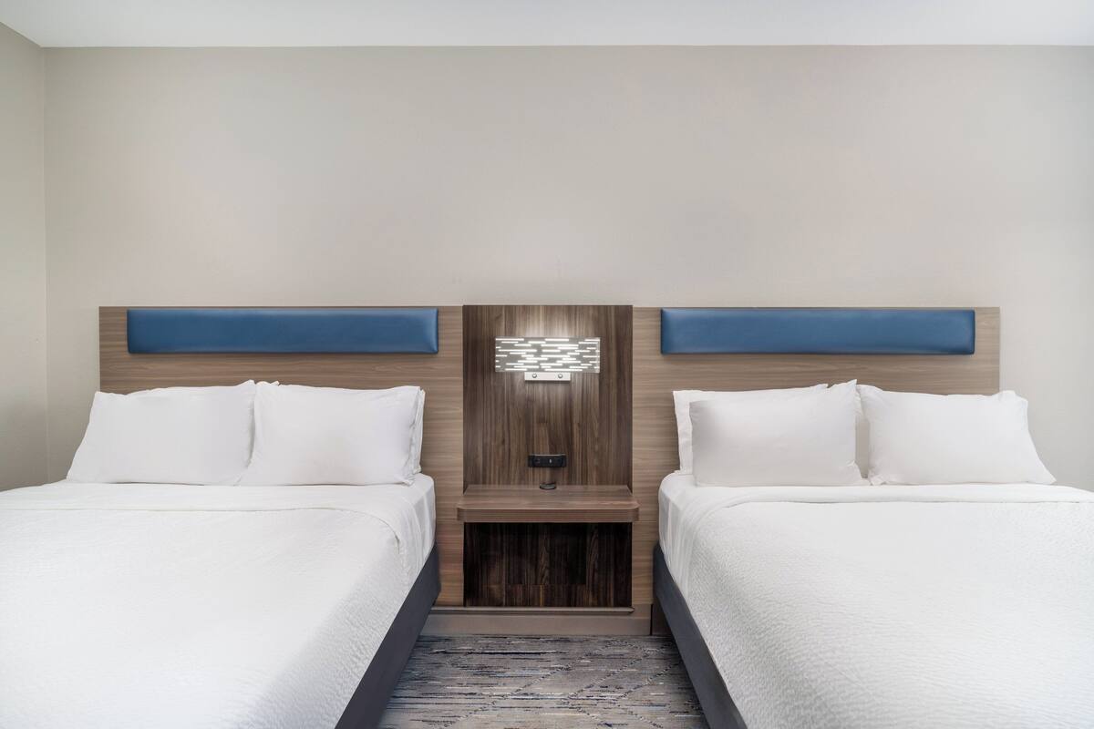 A hotel room with two beds, a wooden headboard, and a small table between them.