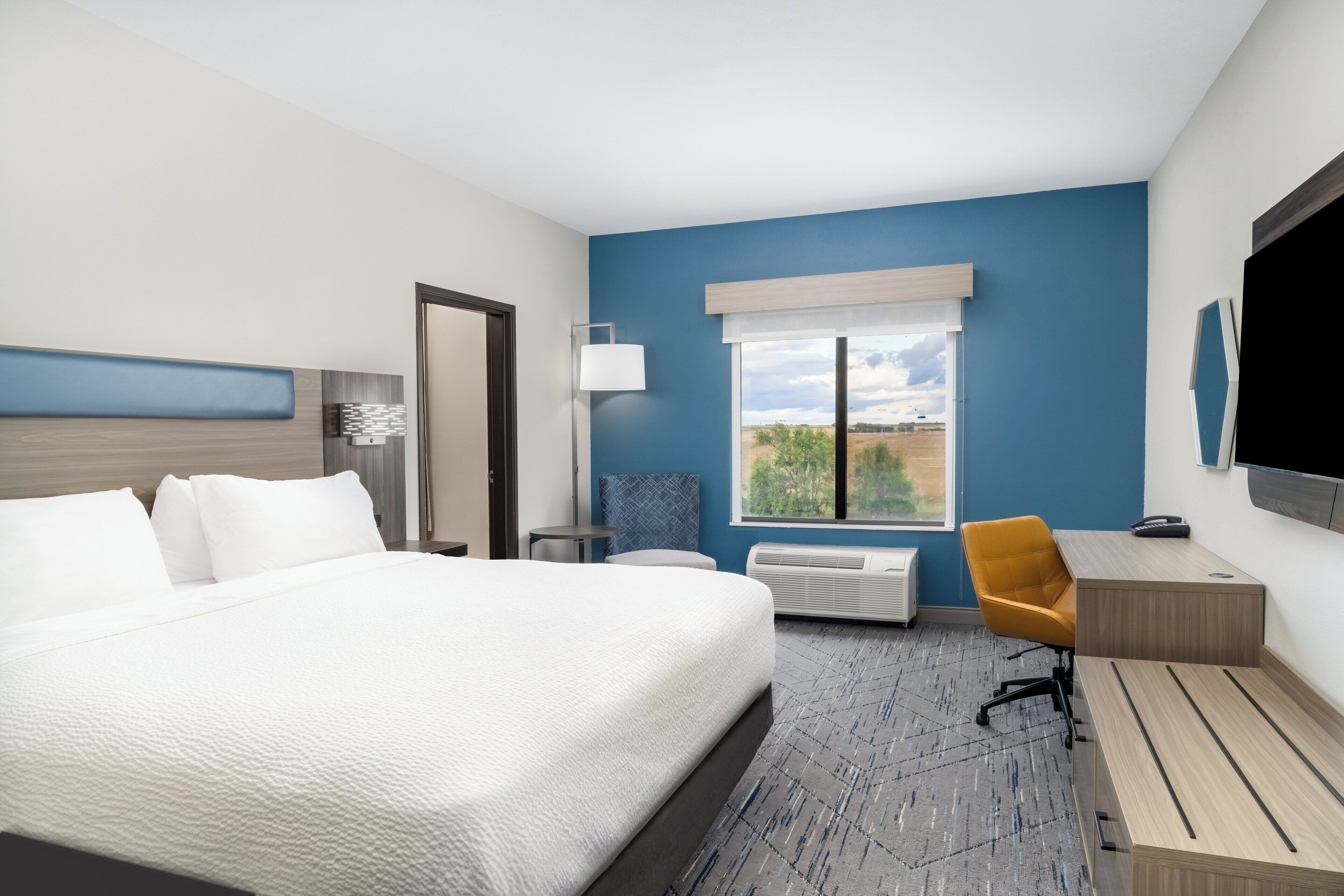 A hotel room with a large bed, a desk, a chair, a flat-screen TV, and a window with a view of the outdoors.
