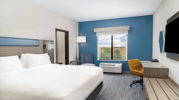 A hotel room with a large bed, a desk, a chair, a flat-screen TV, and a window with a view of the outdoors.