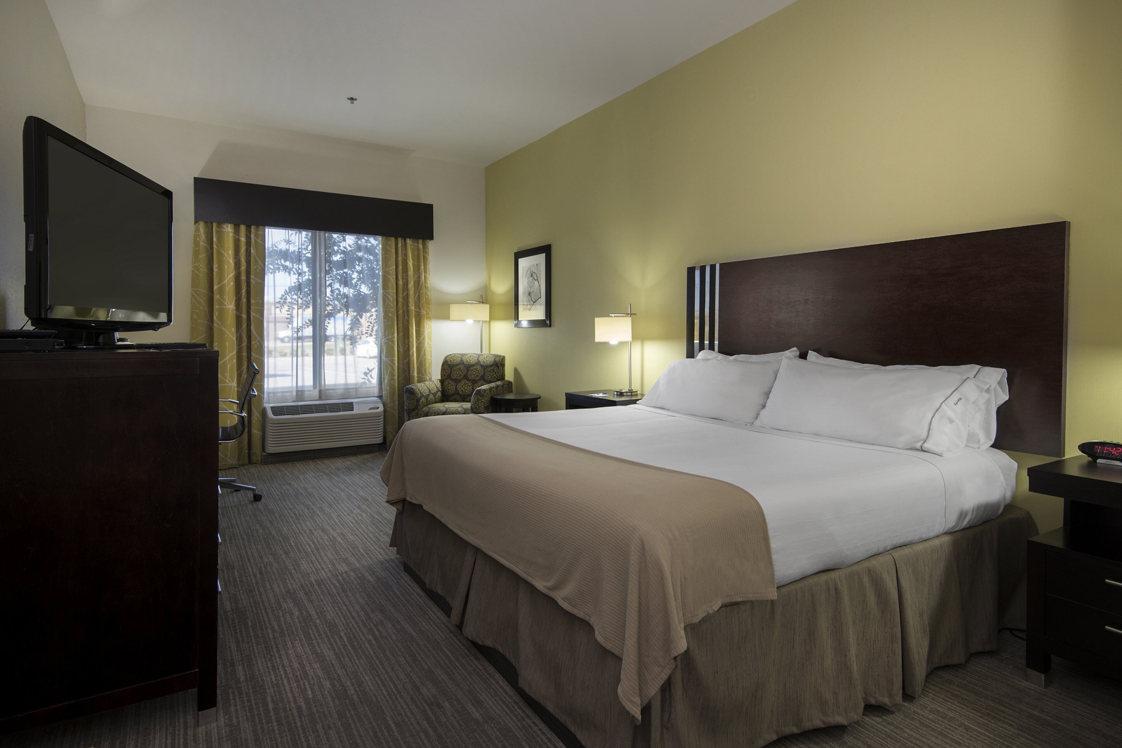 Quarto de hotel com uma cama grande, televisão, escrivaninha e uma cadeira.