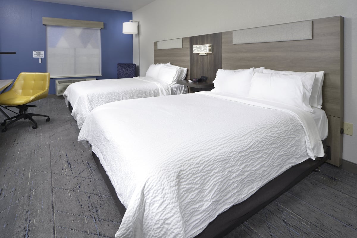 A hotel room with two beds, a chair, and a window with blinds.