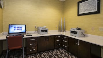 A hotel room with a desk, computer, printer, and a framed picture on the wall.