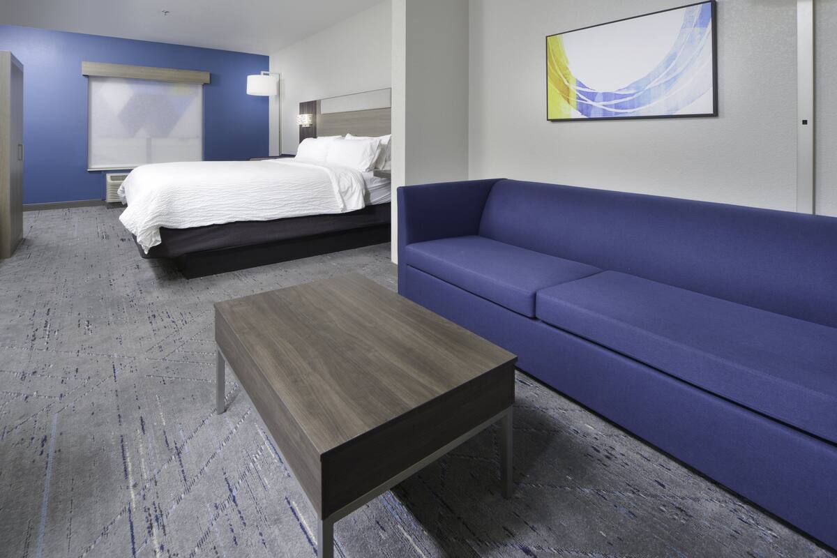 A hotel room with a bed, a blue sofa, and a wooden coffee table.