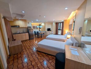 A hotel room with a kitchenette, two beds, a dining area, and a bathroom. - Prince Plaza II Hotel (Makati)