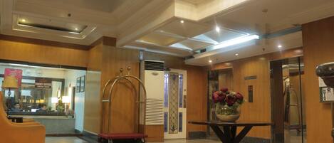 A lobby with a reception desk, a red elevator, and a flower vase on a table.