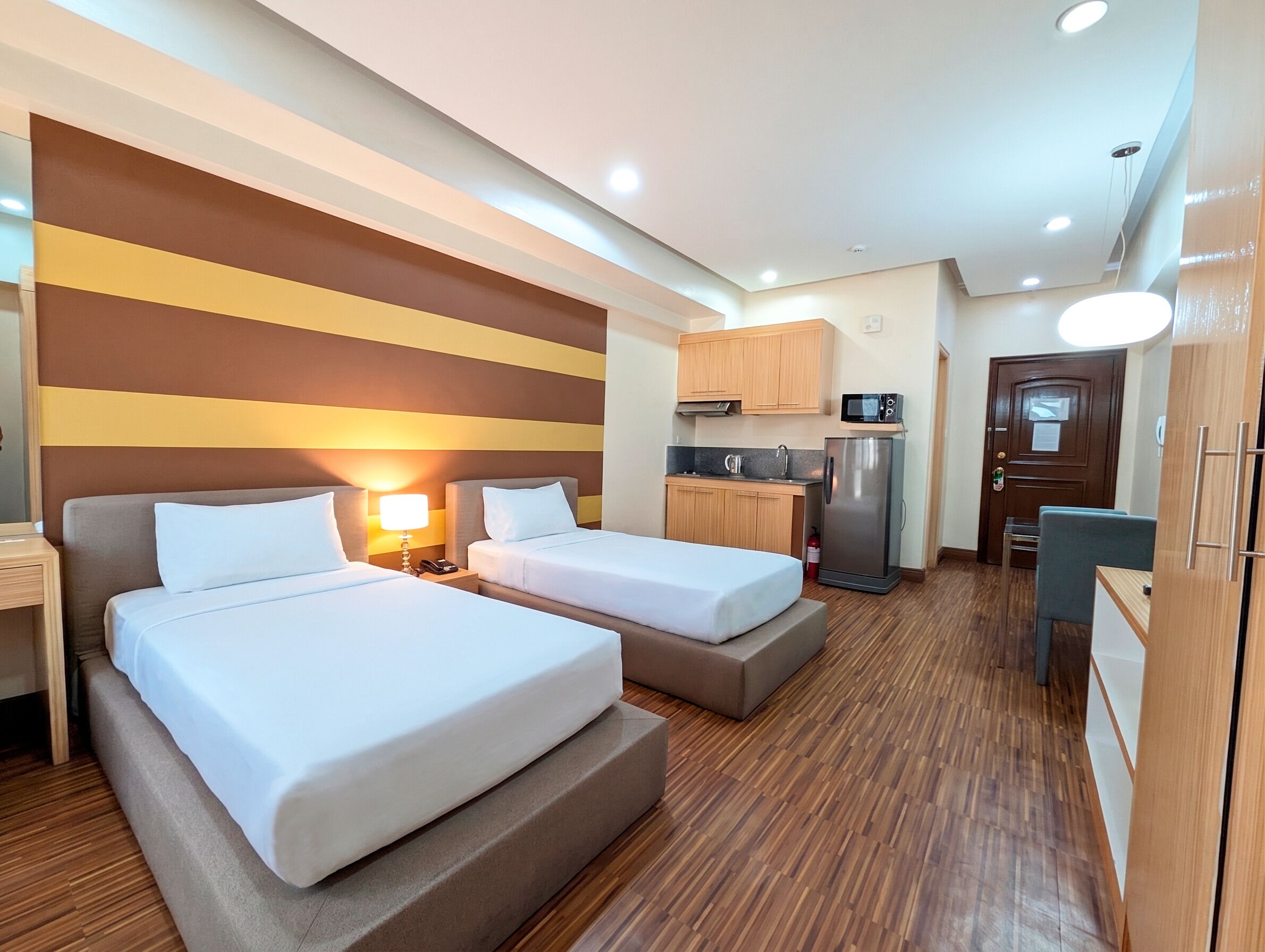 A hotel room with two beds, a kitchenette, a microwave, a refrigerator, and a wooden floor.