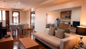 A hotel room with a sofa, a TV, a desk, a lamp, and a kitchenette. - Prince Plaza II Hotel (Makati)