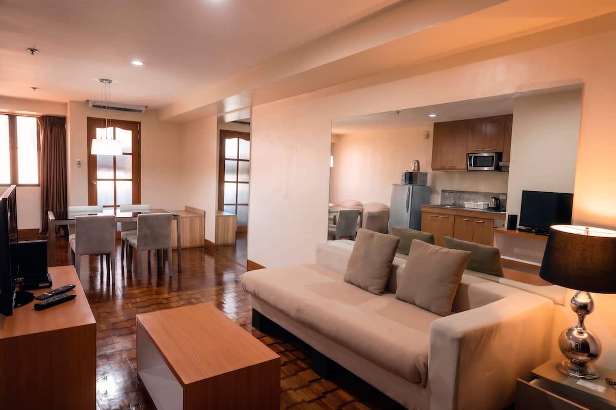 A hotel room with a sofa, a TV, a desk, a lamp, and a kitchenette.