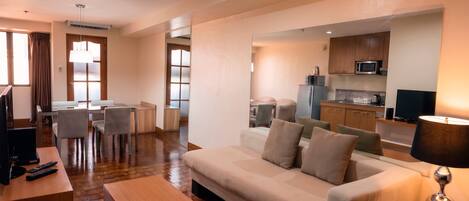 A hotel room with a sofa, a TV, a desk, a lamp, and a kitchenette.