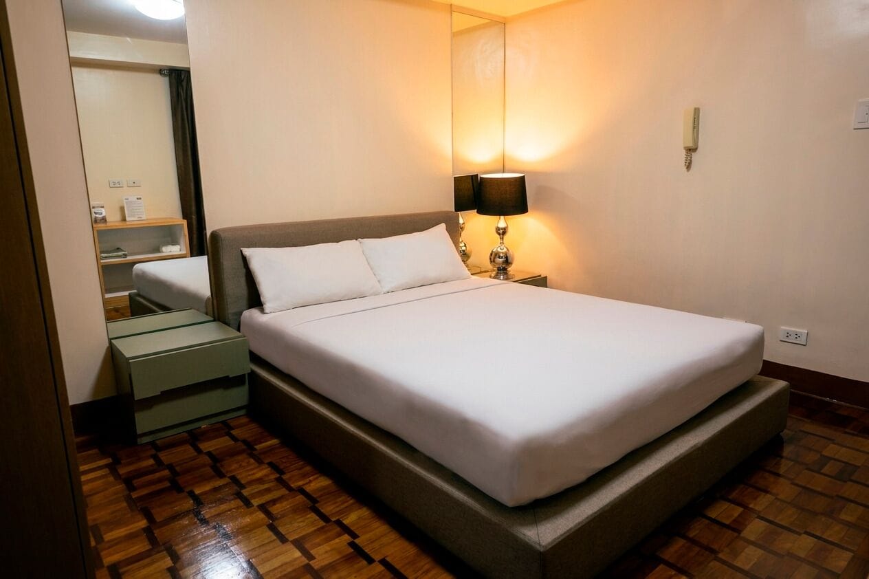 Una habitación de hotel con cama, lámpara de noche, mesita de noche y un espejo.