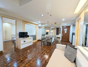A modern hotel room with a wooden floor, a sofa, a TV, a dining area, and a wooden wardrobe. - Prince Plaza II Hotel (Makati)