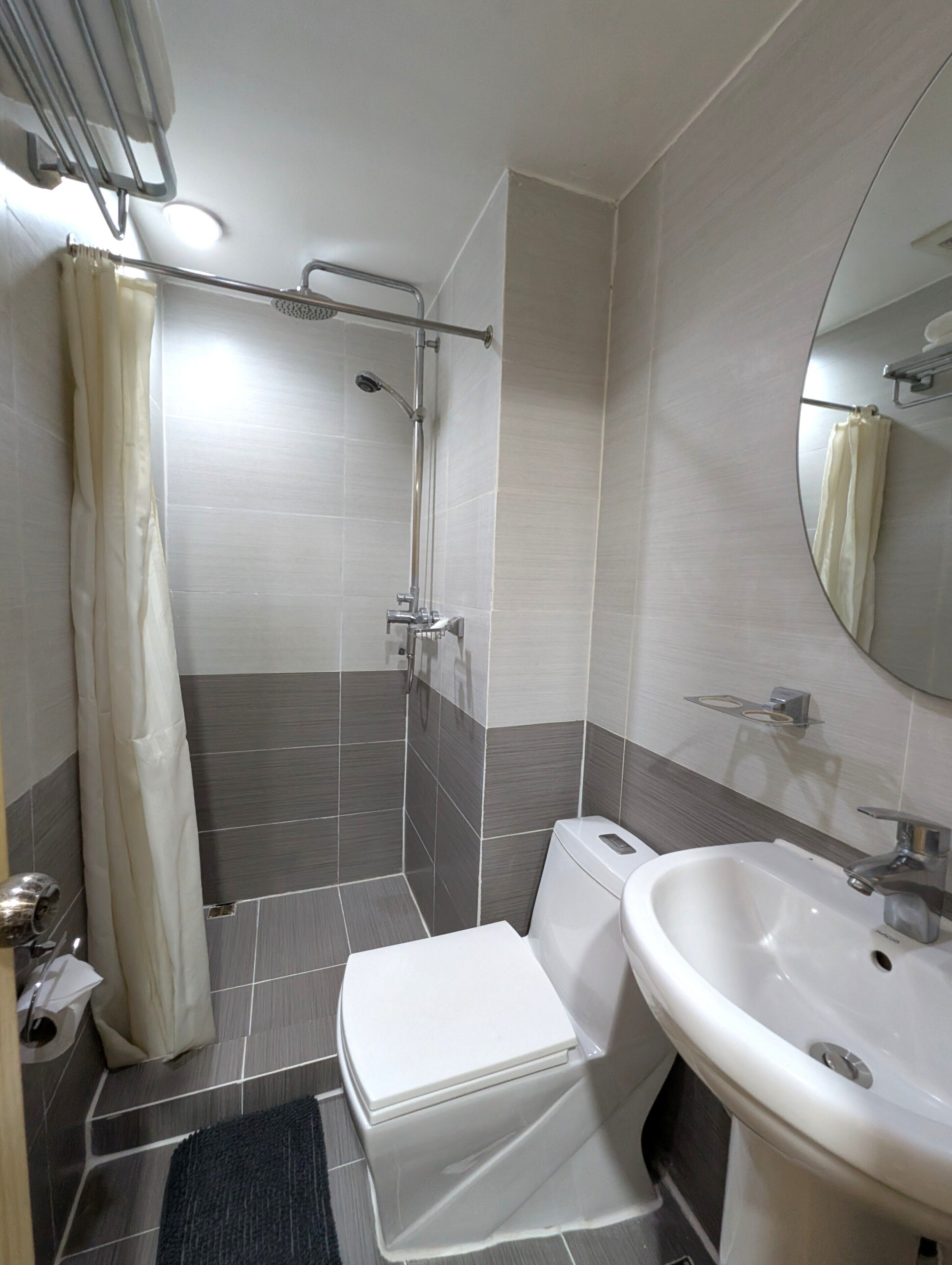 A bathroom with a shower, toilet, sink, and a mirror.