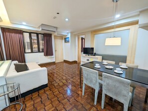 A hotel room with a sofa, a dining table with chairs, a TV, and an air conditioning unit. - Prince Plaza II Hotel (Makati)