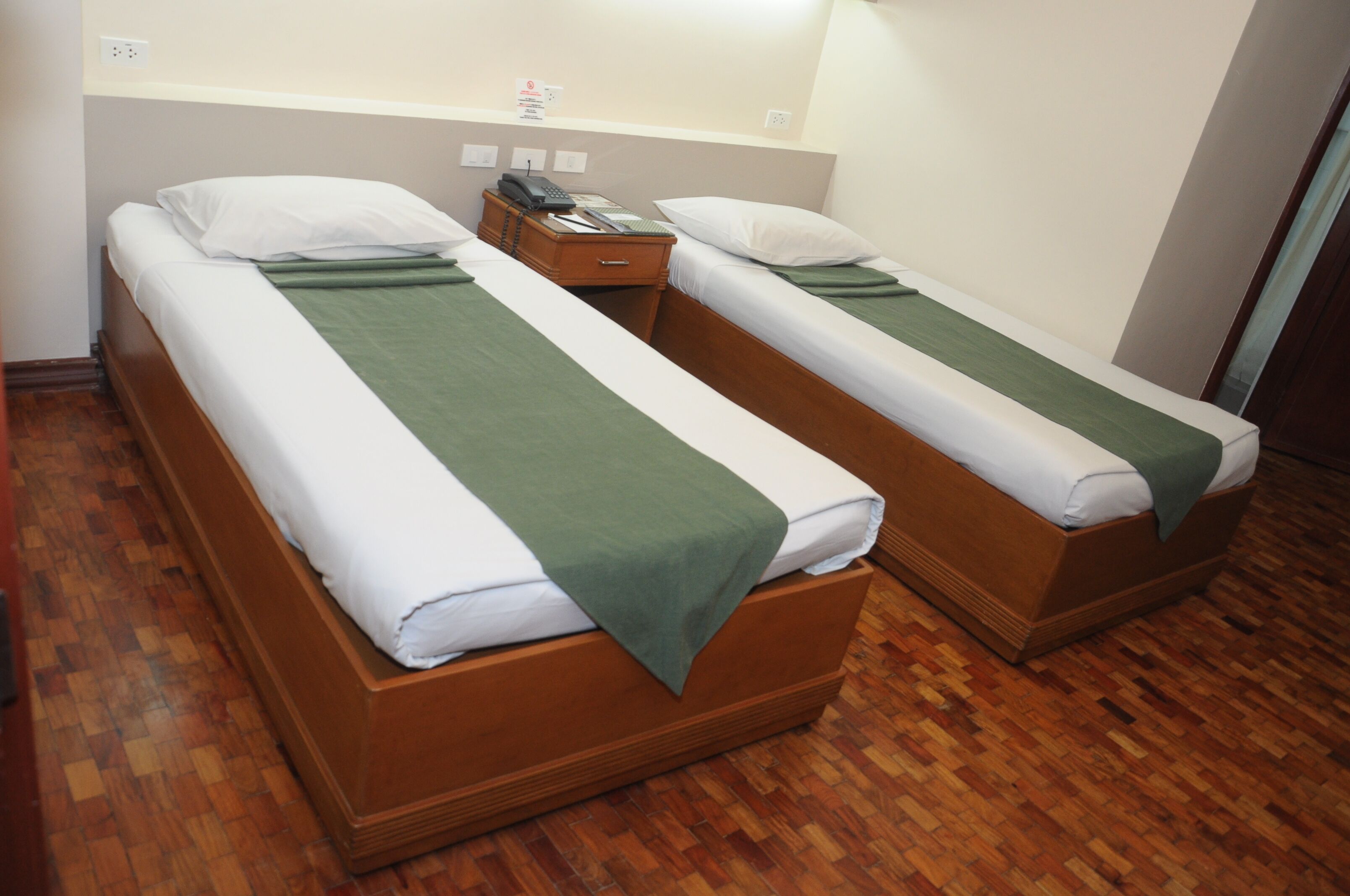 Two single beds with wooden frames, white bedding, and green throw blankets.