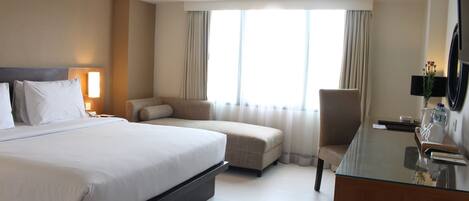 A hotel room with a large bed, a sofa, a desk, and a TV.