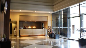 Zona de recepción de un hotel con mostrador de entrada, una recepcionista y un amplio ventanal hacia el exterior.
