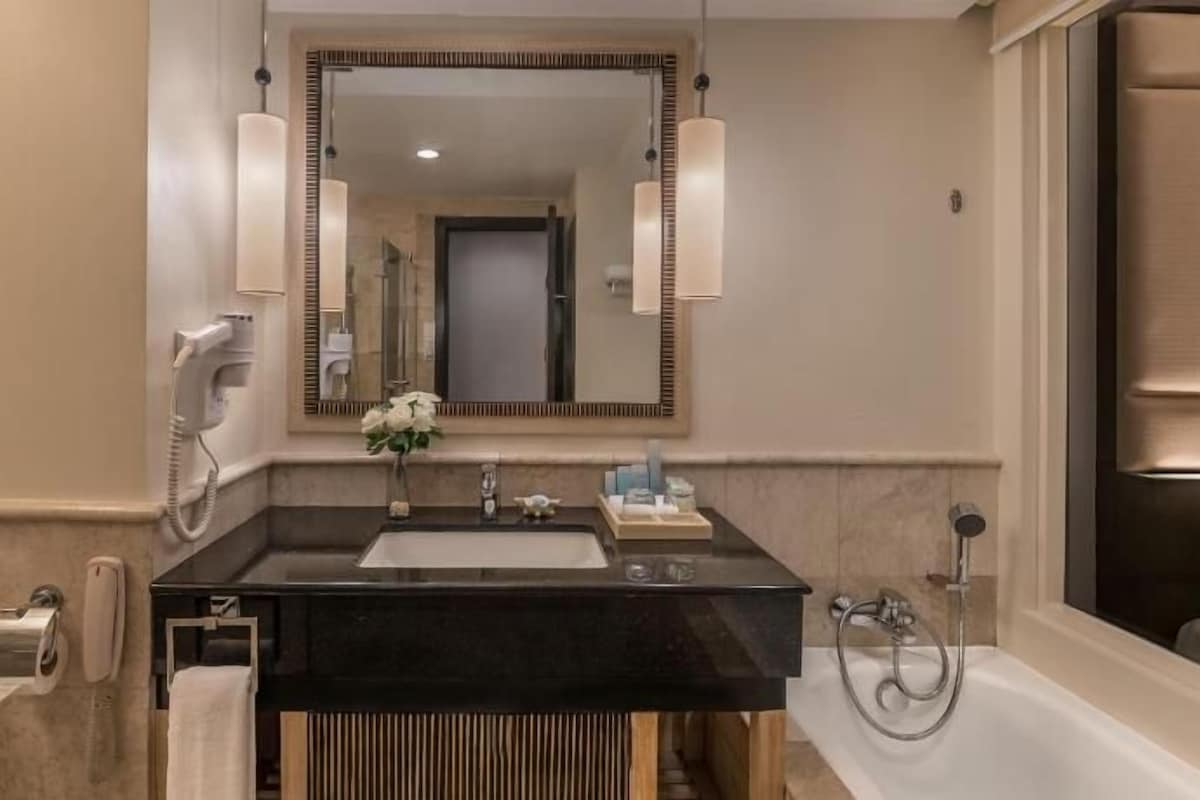Un baño moderno con un lavamanos negro, un espejo grande y una bañera.