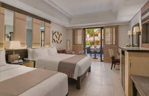 Habitación de hotel con dos camas, un escritorio, una silla, una mesa de comedor y un balcón con vistas a palmeras.