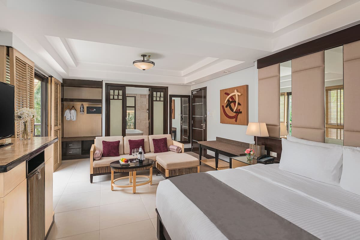 Habitación de hotel con cama, escritorio, sofá, televisión y baño visible a través de una puerta abierta.