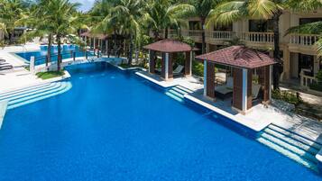 A large swimming pool surrounded by palm trees and a building with balconies.