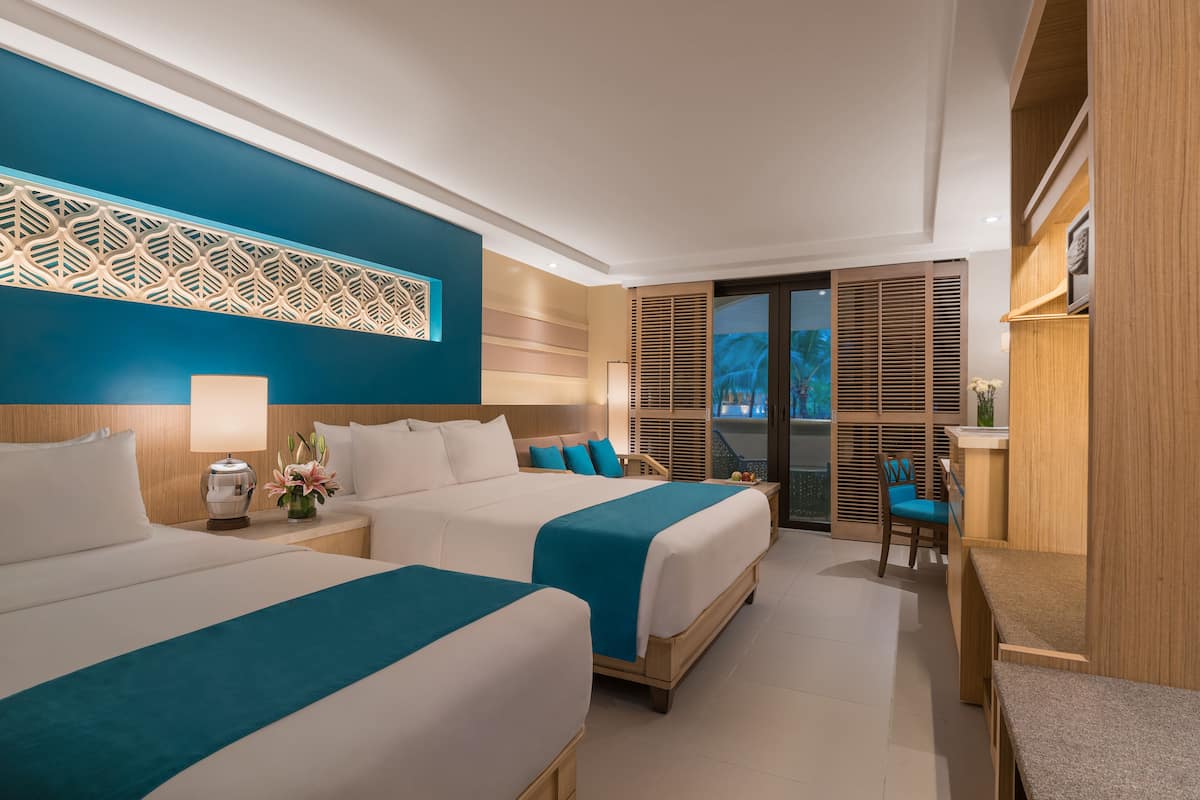 Habitación de hotel con dos camas, un escritorio y vistas al exterior.