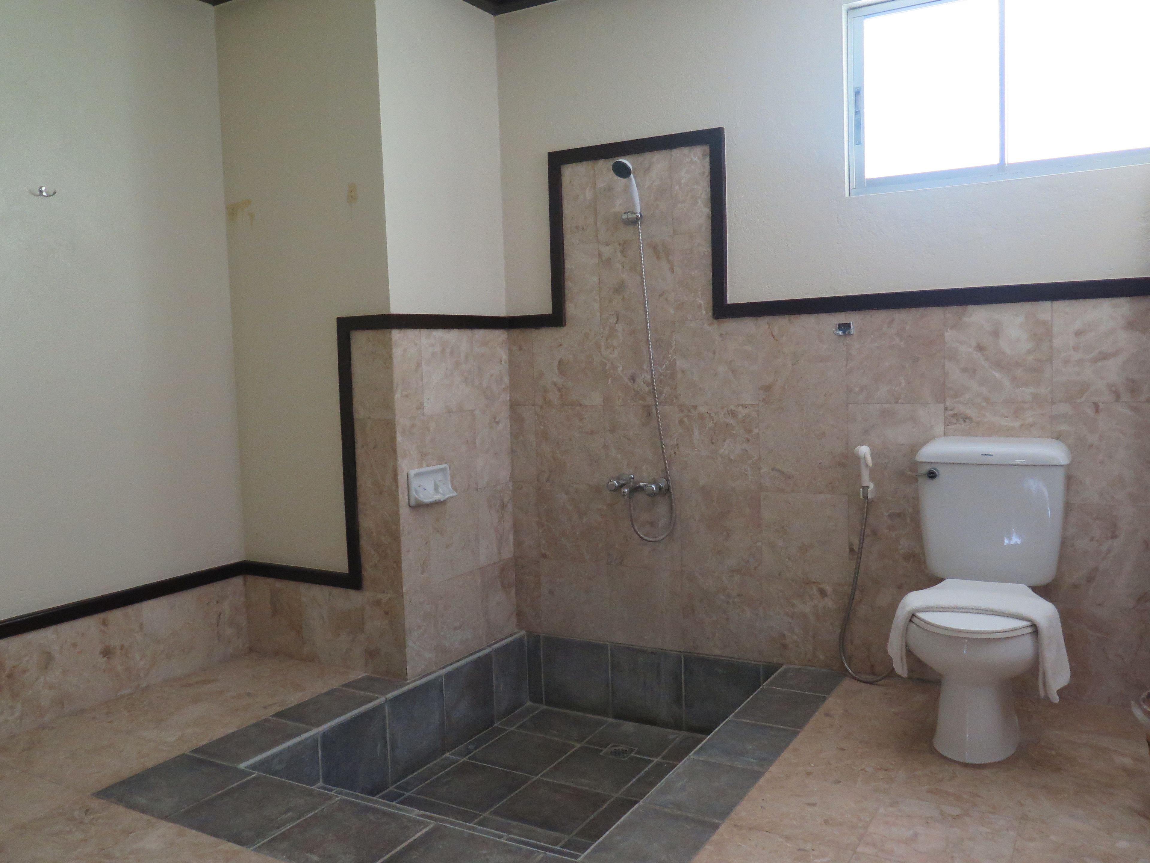 Ein Badezimmer mit Dusche, Toilette und Fliesenboden.