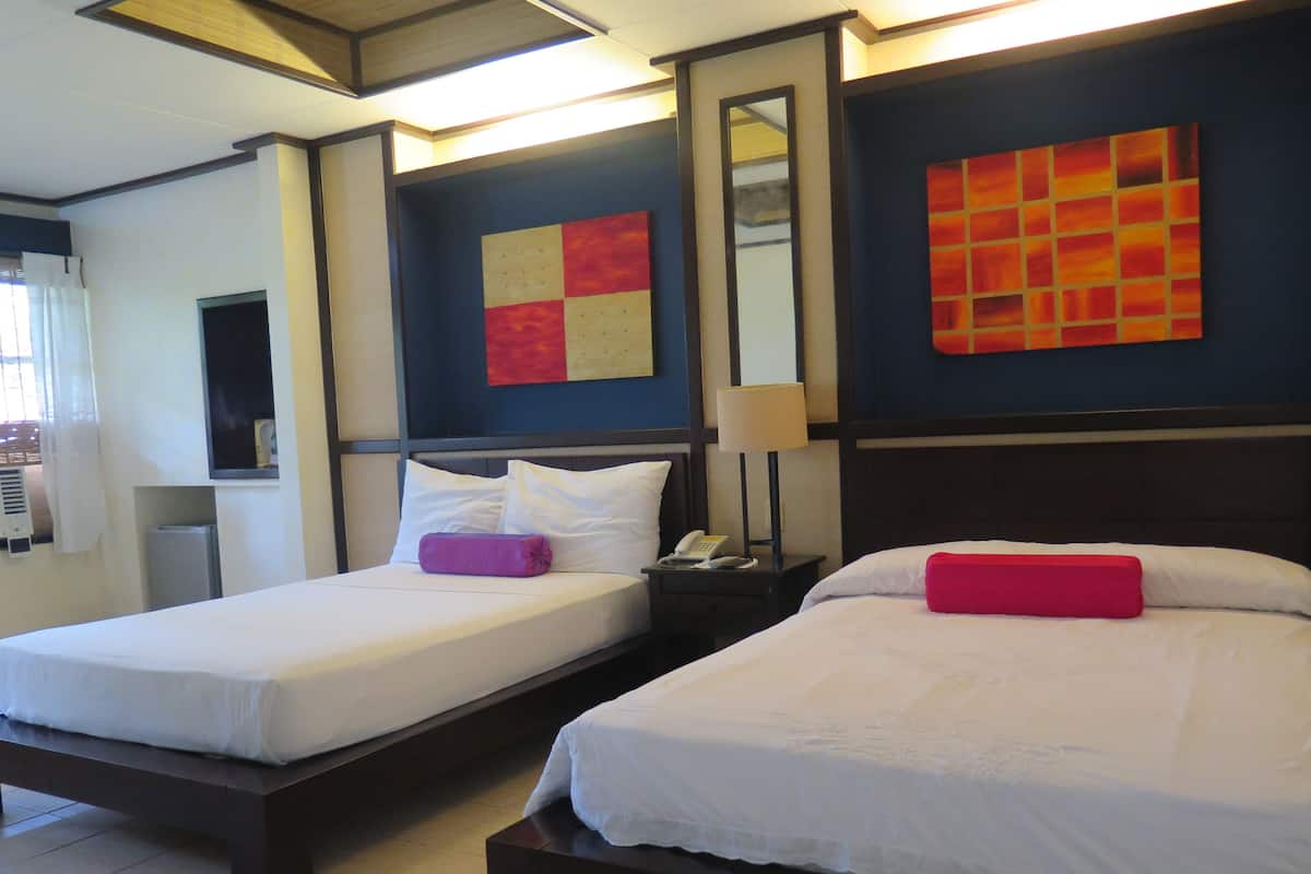 A hotel room with two single beds, a nightstand with a lamp, a phone, and a wall-mounted mirror.