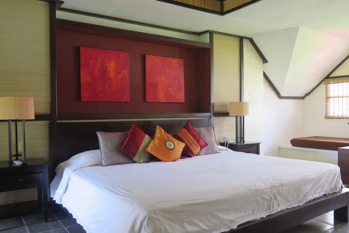 A hotel room with a large bed, two nightstands, a wooden headboard, and red artwork on the wall.