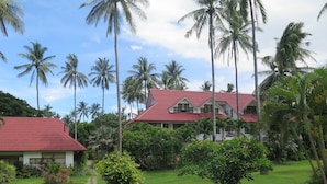 A two-story building with a red roof, surrounded by lush greenery and palm trees. - Bahura Resort and Spa (Zamboanguita)