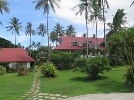 A two-story building with a red roof, surrounded by lush greenery and palm trees.